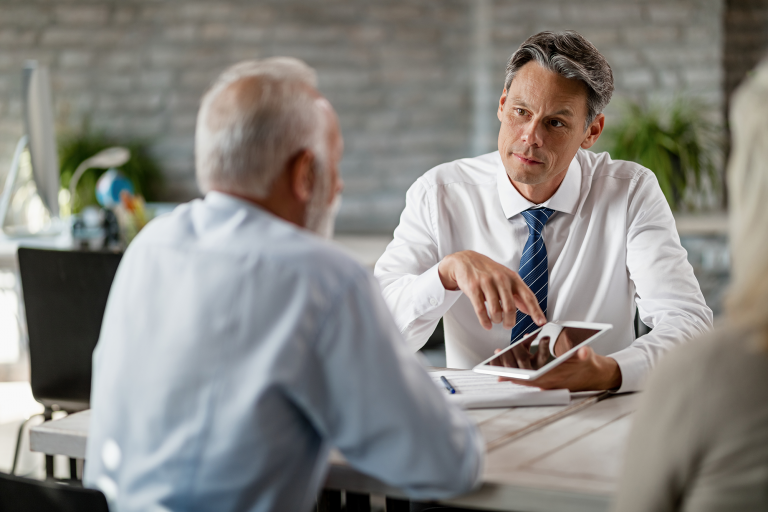 Conseiller qui présente des documents sur une tablette à un couple de clients lors d'un rendez-vous