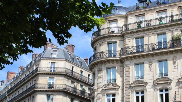 Façades d'immeubles haussmanniens à balcons de fer forgé sous un ciel bleu
