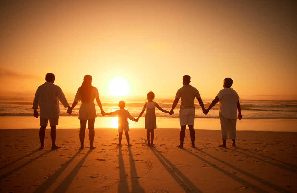 Famille se tenant par la main sur une plage, face au soleil couchant